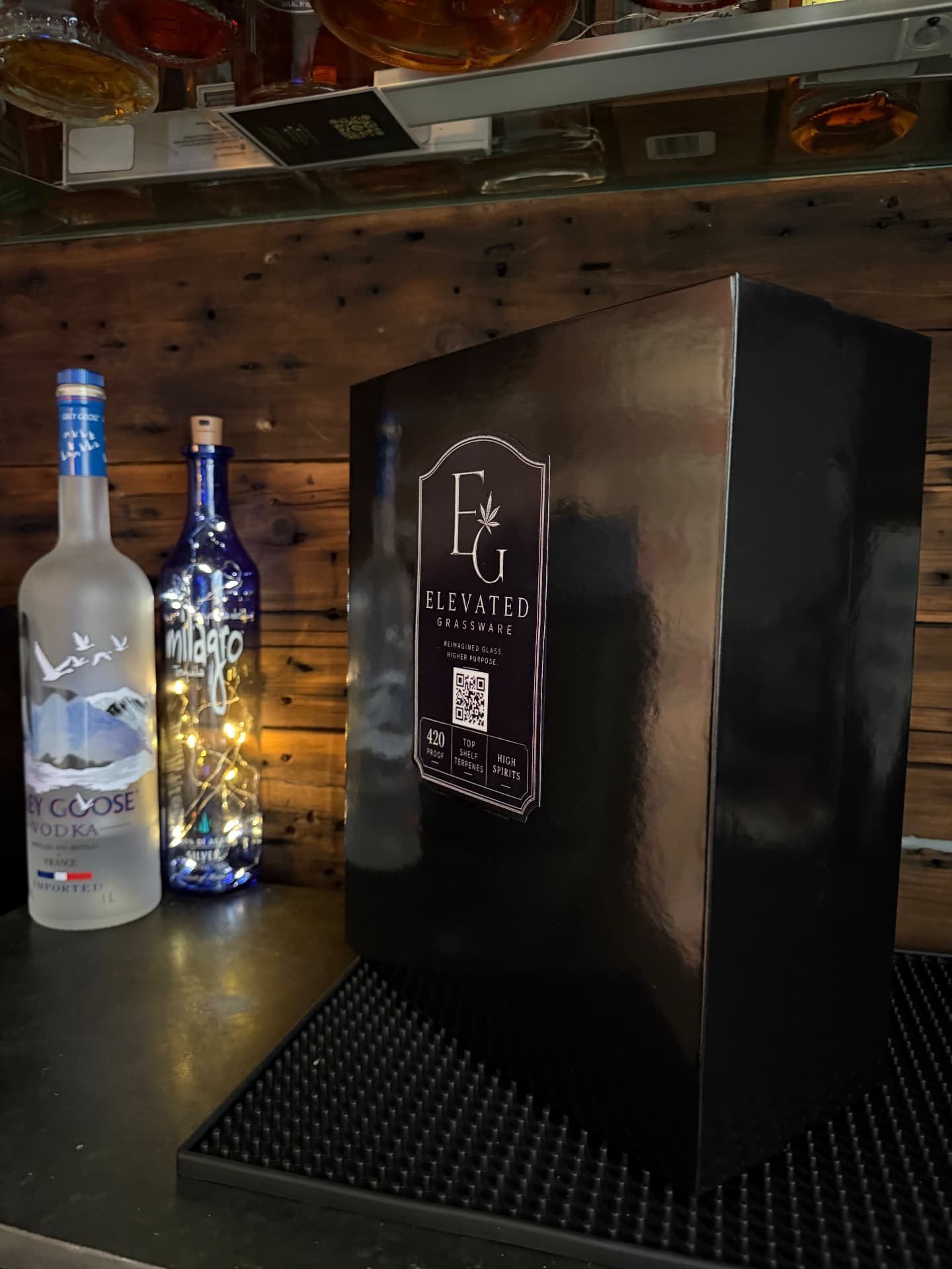 Sealed Elevated Grassware box sitting on a back bar beside liquor bottles